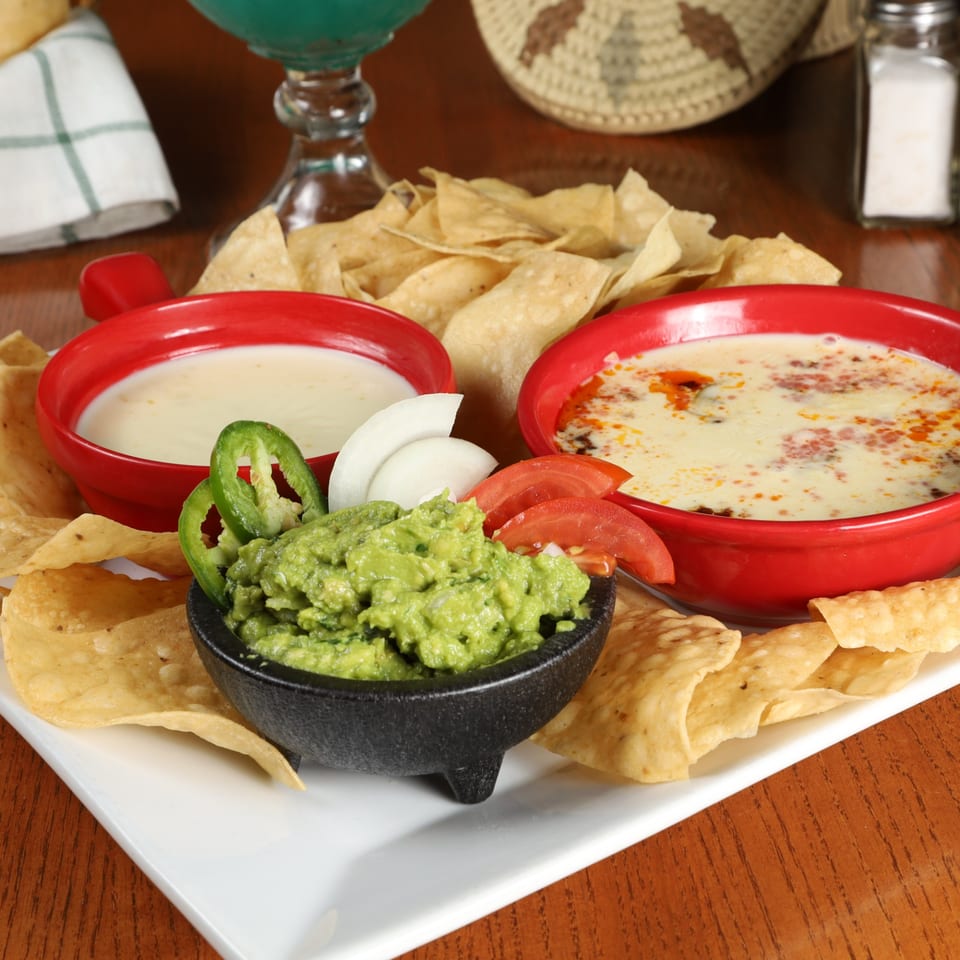 La Fuente Mexican Bar & Grill's chips, guacamole, and two bowls of queso dip on a white platter.