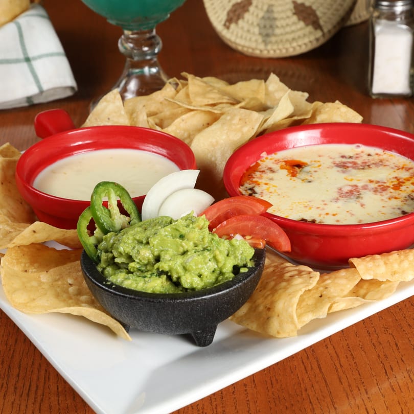 La Fuente Mexican Bar & Grill's chips, guacamole, and two bowls of queso dip on a white platter.