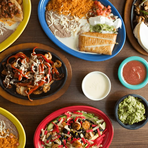 Overhead view of several colorful plates of Mexican food, including fajitas, rice, beans, and salad.