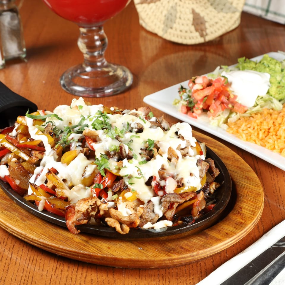 Sizzling fajitas with melted cheese and cilantro, served with rice, guacamole, and pico de gallo.