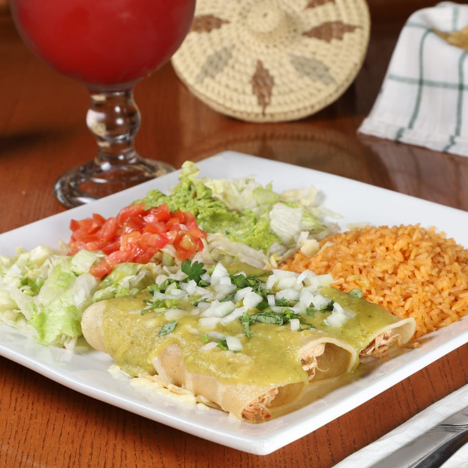 Two chicken enchiladas with green sauce, rice, lettuce, and tomatoes on a white plate.