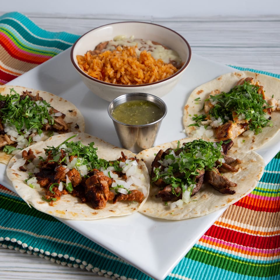 Four La Fuente Mexican Bar & Grill tacos with rice, beans, and green salsa on a colorful striped placemat.