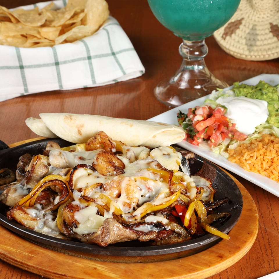 Sizzling fajitas with melted cheese, bell peppers, and onions, served with tortillas, rice, and guacamole.